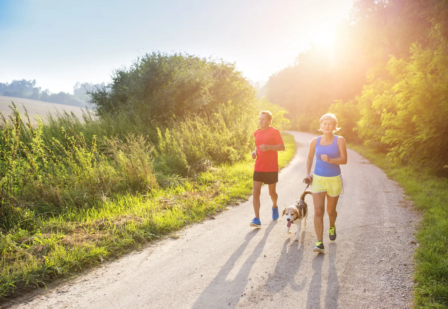 Male and female runners jogging on a paved trail with a small dog